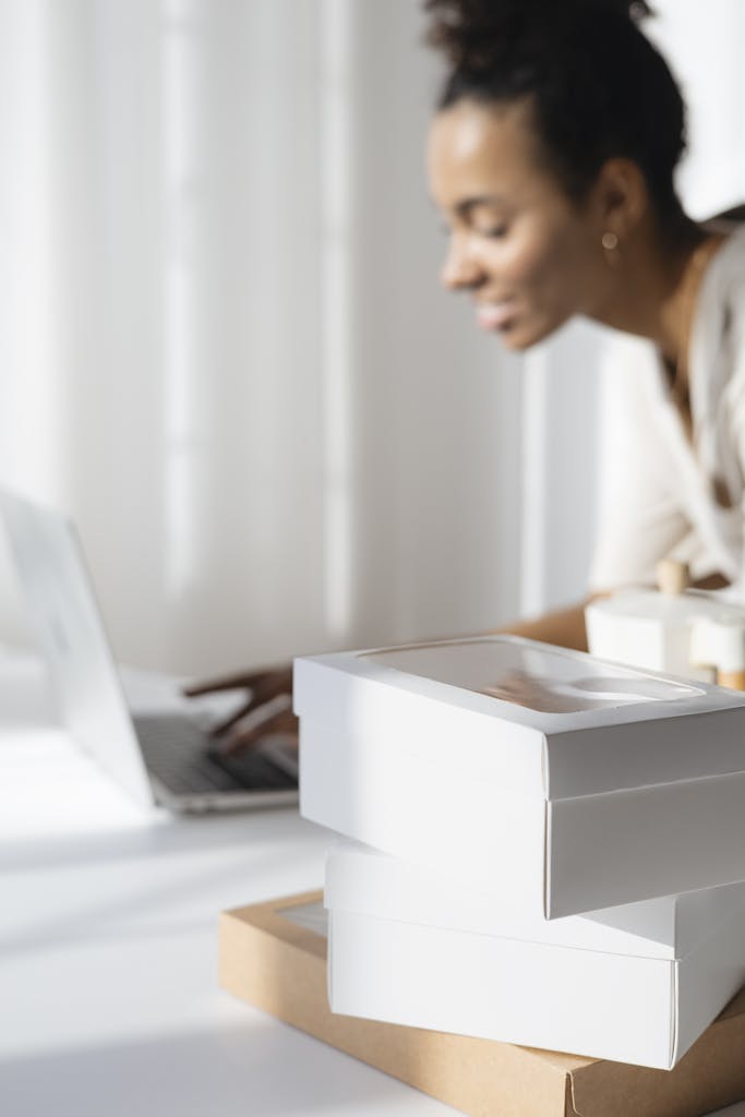 A focused woman planning her bakery business with a laptop and packaging boxes.